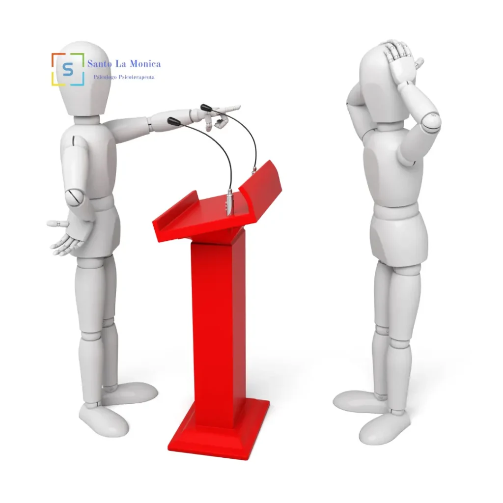 Manichino che accusa puntando il dito verso un altro manichino in difficoltà, vicino a un podio rosso con microfoni: rappresentazione dell’autocritica eccessiva.