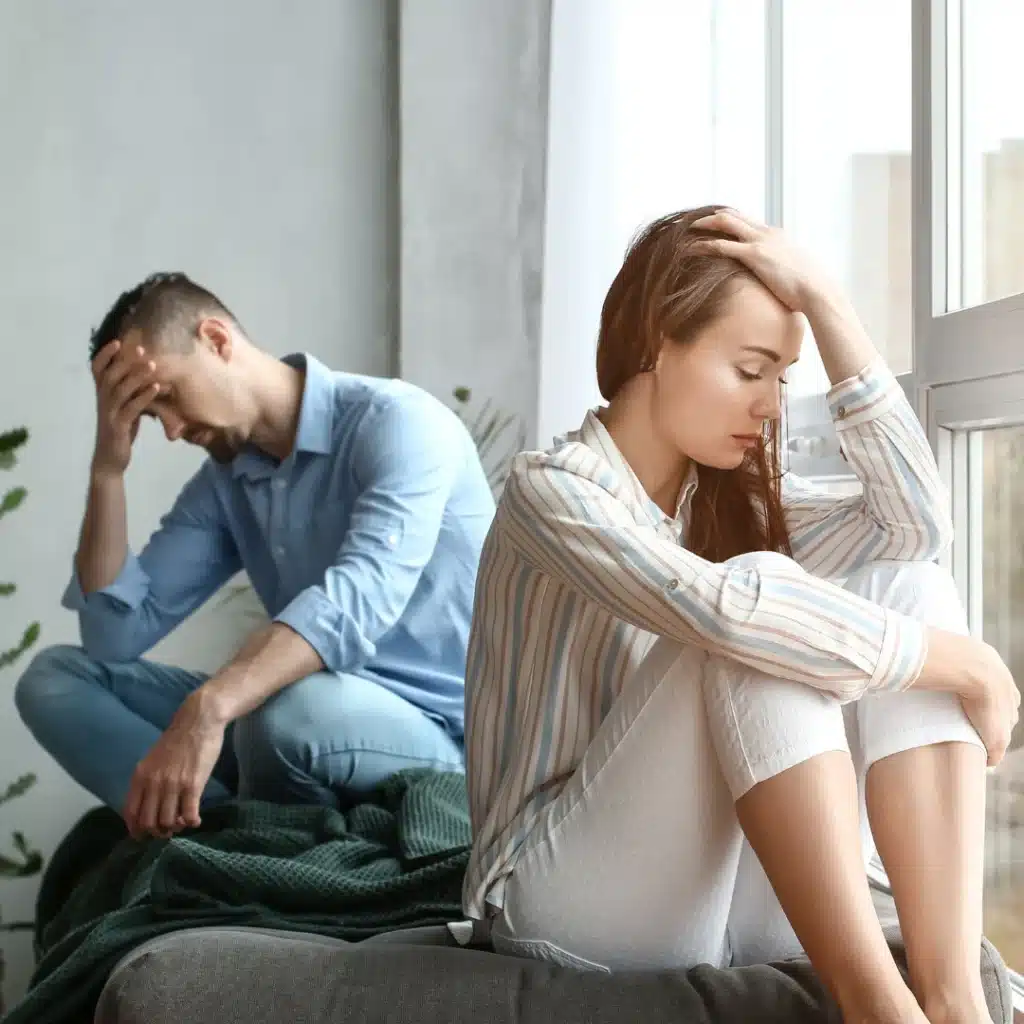 Coppia seduta in casa in atteggiamento triste e pensieroso dopo la fine di una relazione.