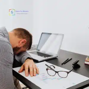 Uomo in ufficio con la testa appoggiata sulla scrivania, segni di stanchezza e stress legato al lavoro.