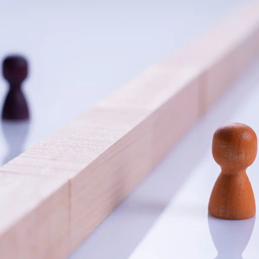 Due pedine in legno separate da una barriera, simbolo di distanza e incomunicabilità nella relazione.