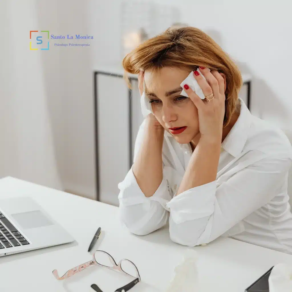 Donna seduta alla scrivania con le mani alla testa, espressione di ansia e stress lavorativo.